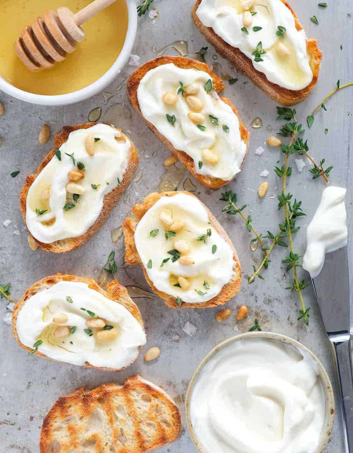 Top view of crostini with whipped ricotta, pine nuts and honey over a grey background,