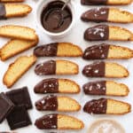 Top view of several chocolate biscotti and melted chocolate in a small bowl over a white background.