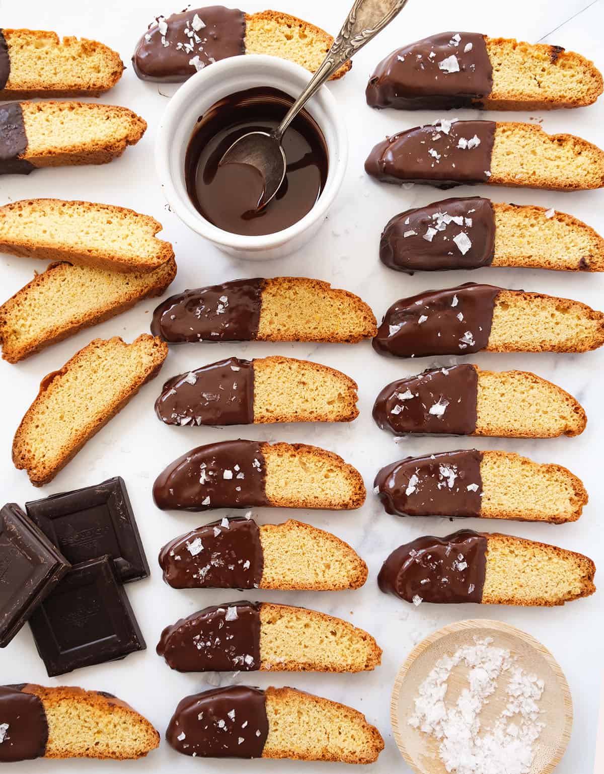 Top view of several chocolate dipped biscotti and melted chocolate in a small bowl over a white background.