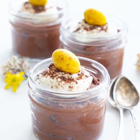 Close-up of three glass mini jars full of easy chocolate mousse over a white background.