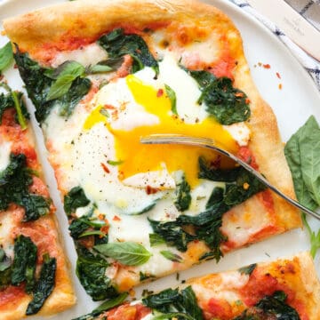 Close-up of a slice of egg pizza topped with spinach and runny egg yolk.