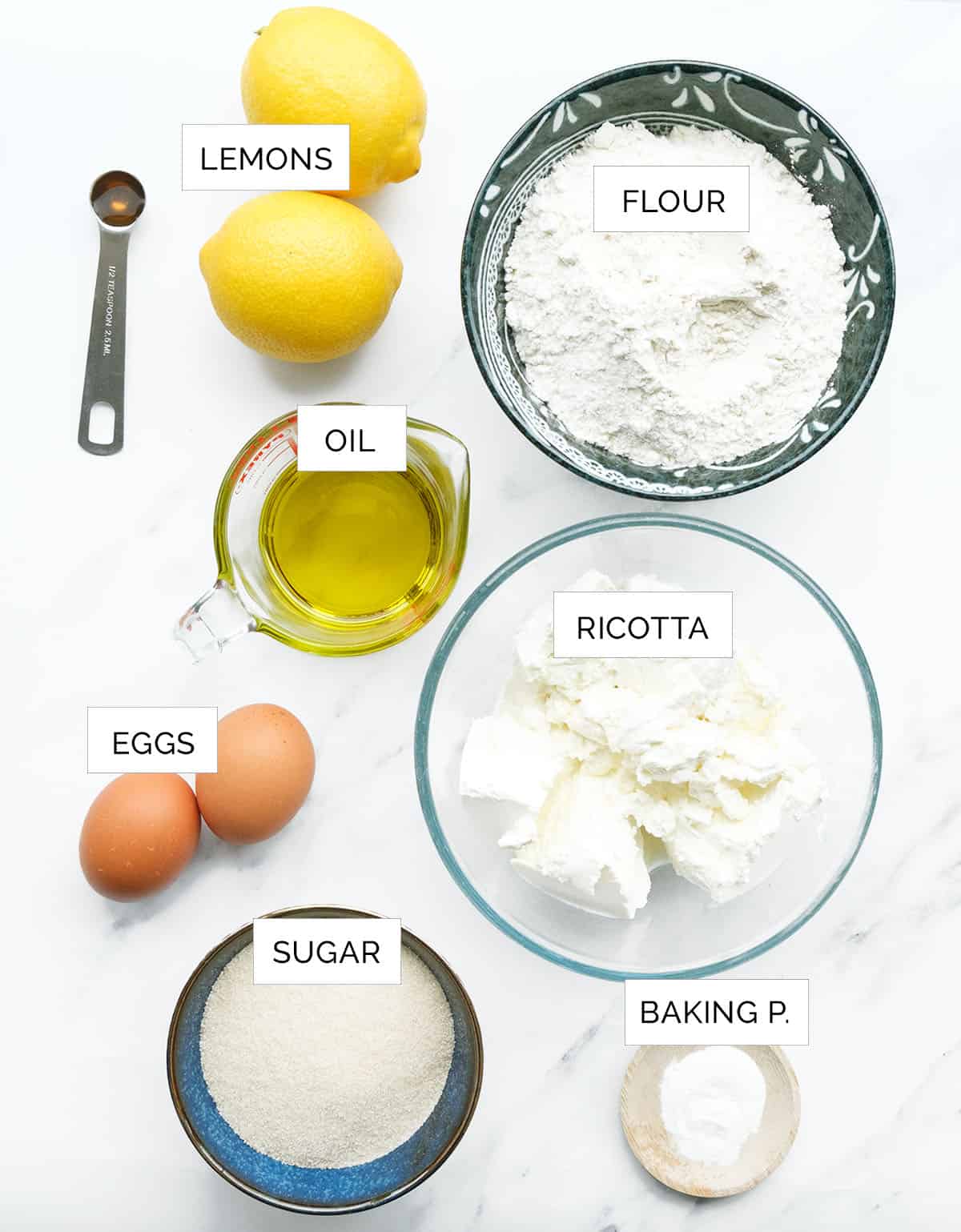 이 레몬 리코타 케이크를 만들기 위한 재료는 흰색 배경 위에 배열되어 있습니다.