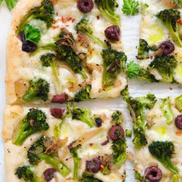 Top view of a large broccoli pizza with kalamata olives cut into slices.