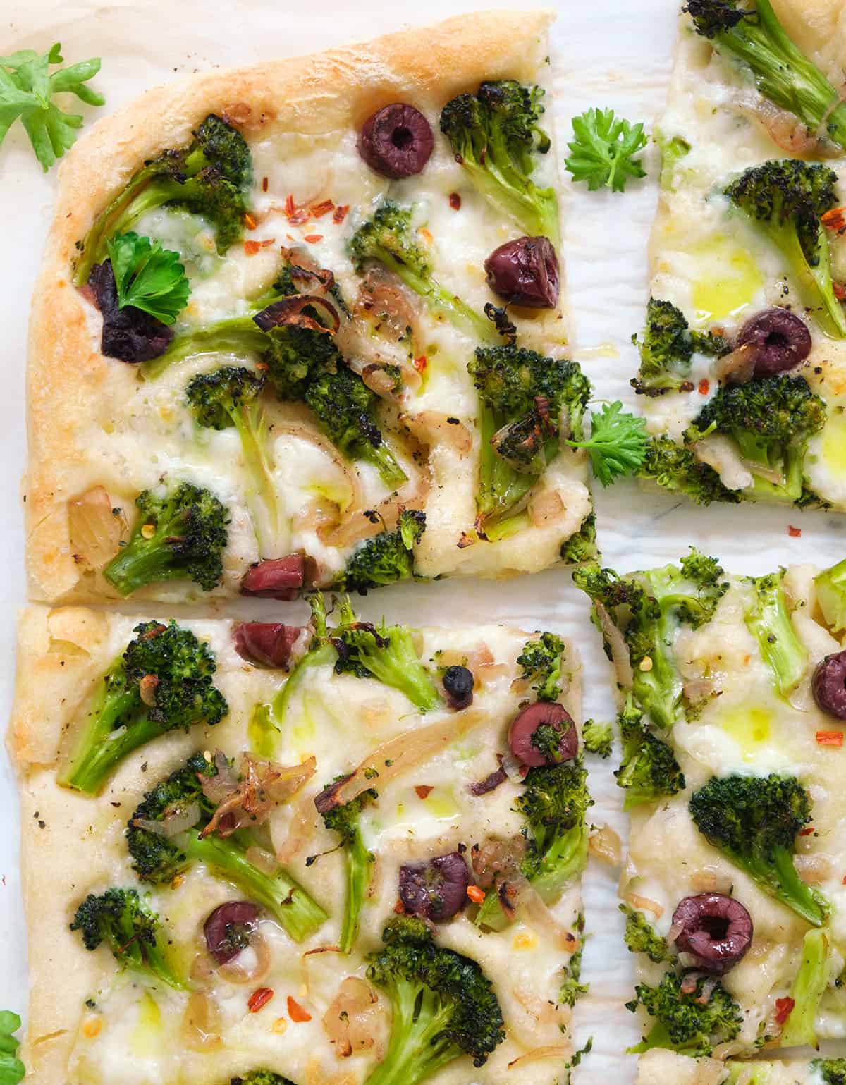 Top view of a large broccoli pizza with black olives cut into slices.