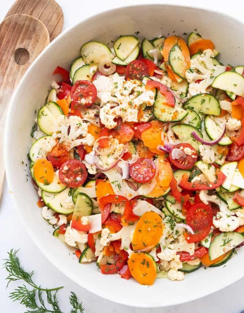 A white salad bowl full of marinated vegetable salad.
