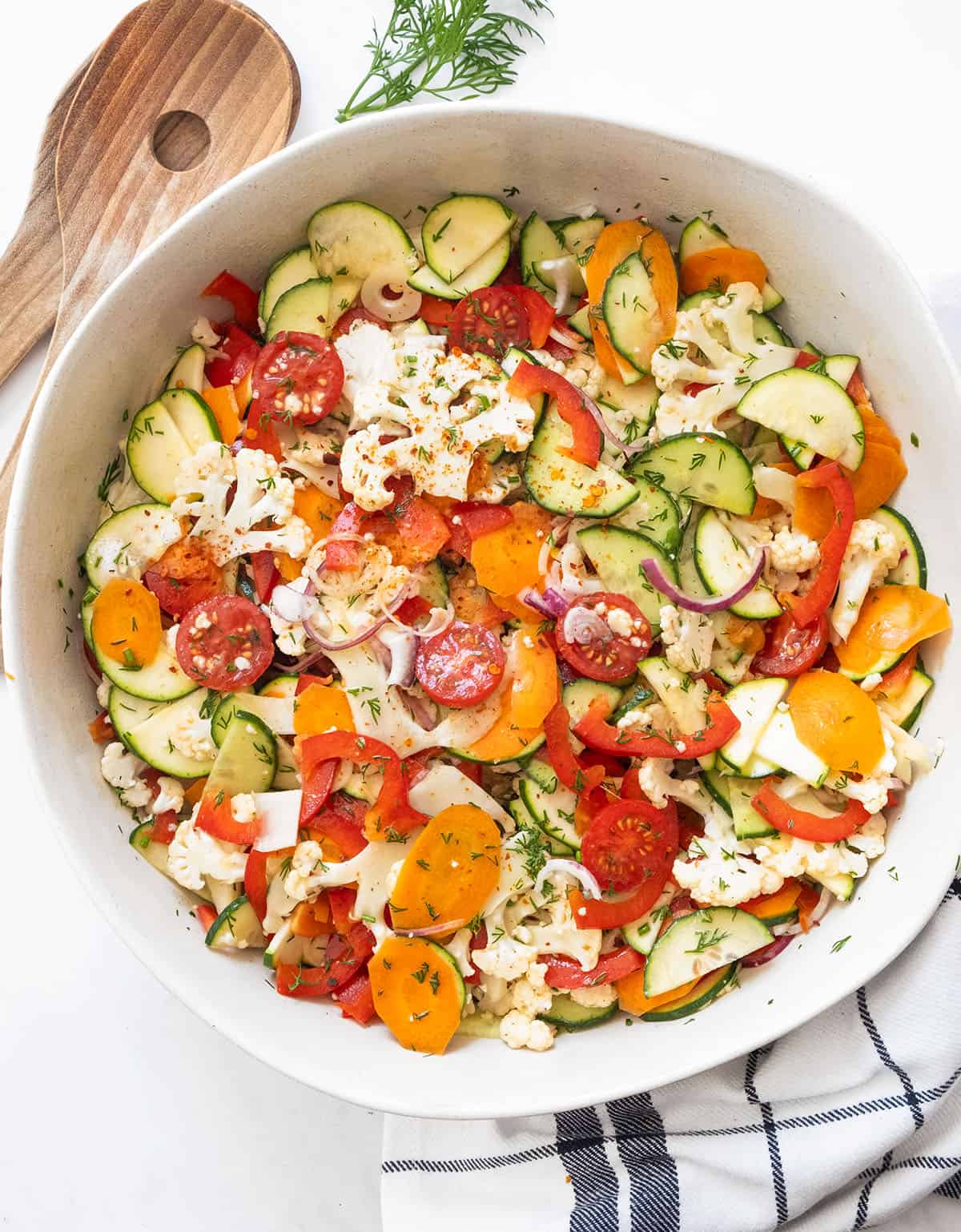 A large white salad bowl full of marinated vegetable salad.