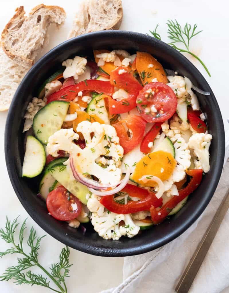 A black bowl with marinated vegetable salad.