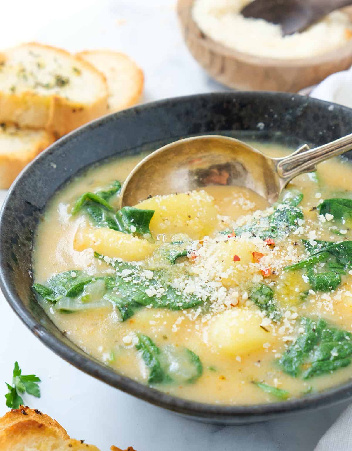 Close-up of a black bowl full of creamy and thick potato spinach soup served with grated parmesan cheese.