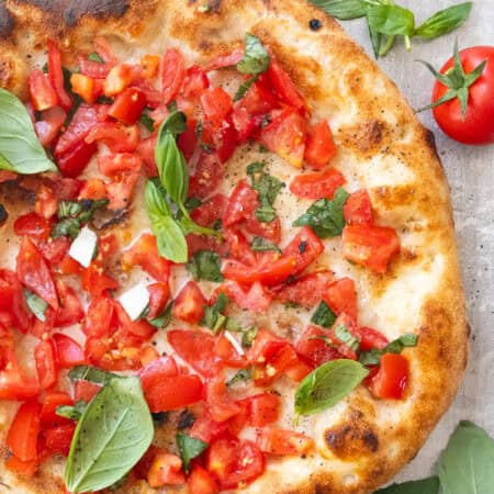 Top view of a large bruschetta pizza with fresh basil leaves.