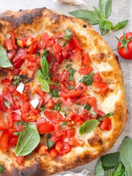 Top view of a large bruschetta pizza with fresh basil leaves.