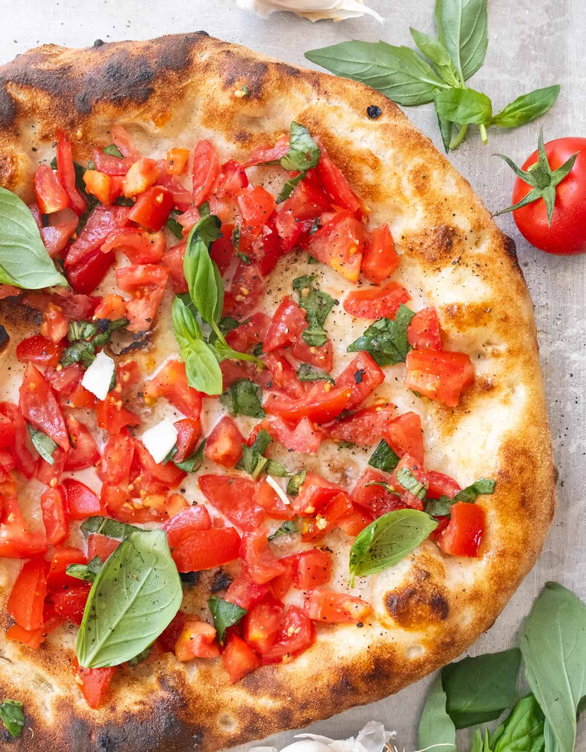 Top view of a round bruschetta pizza topped with diced fresh tomatoes and fresh basil leaves.