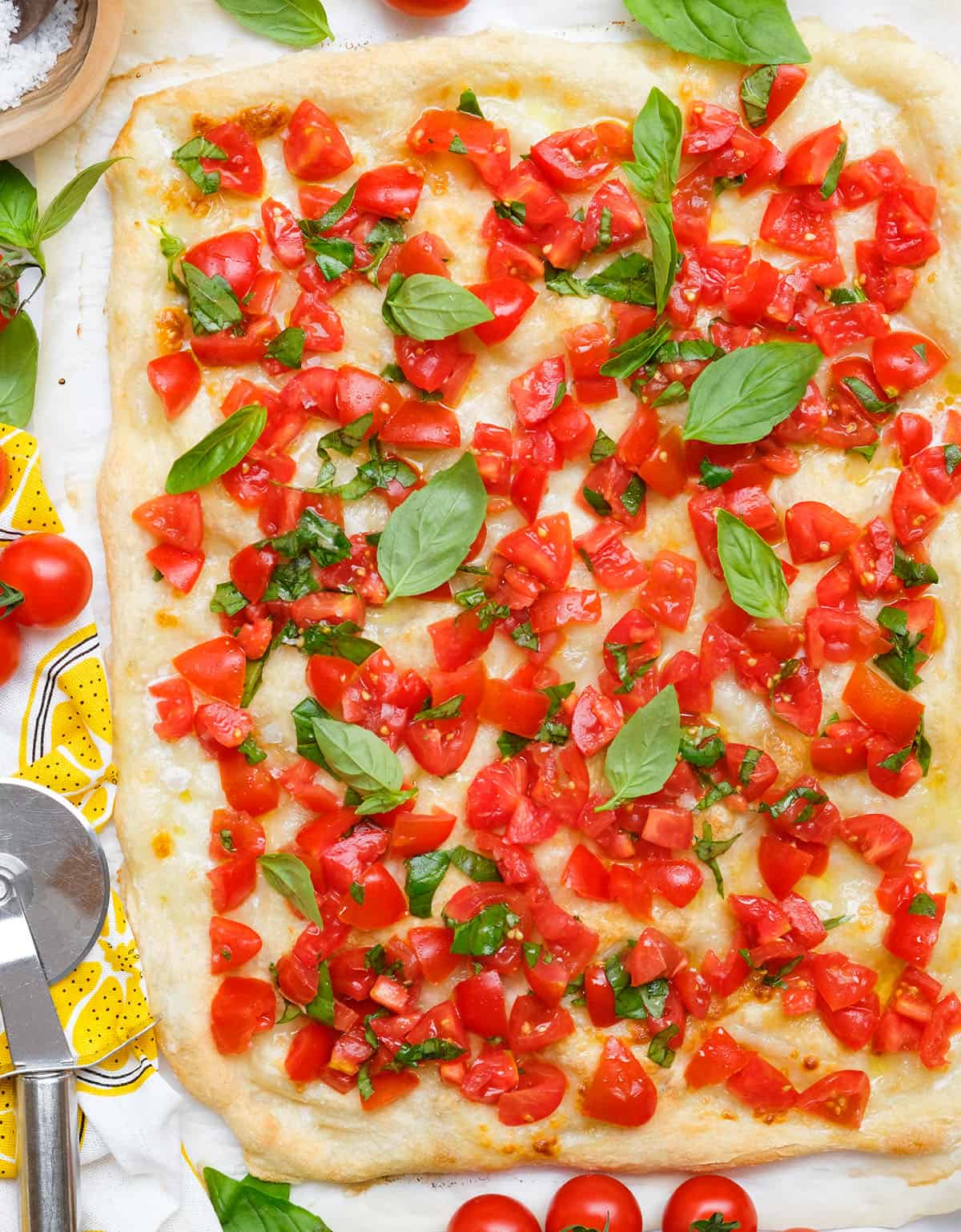 Top view of a large bruschetta pizza topped with diced fresh tomatoes and fresh basil leaves.