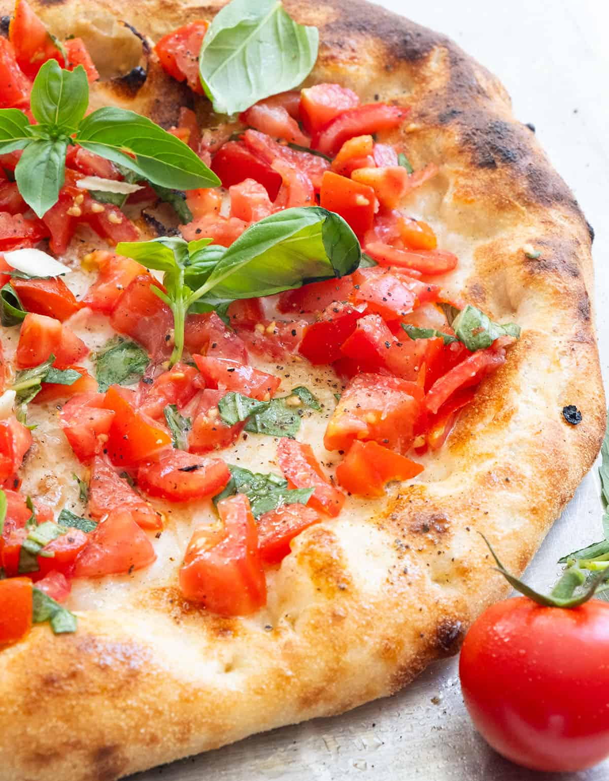 A bruschetta pizza topped with diced fresh tomatoes and fresh basil leaves.