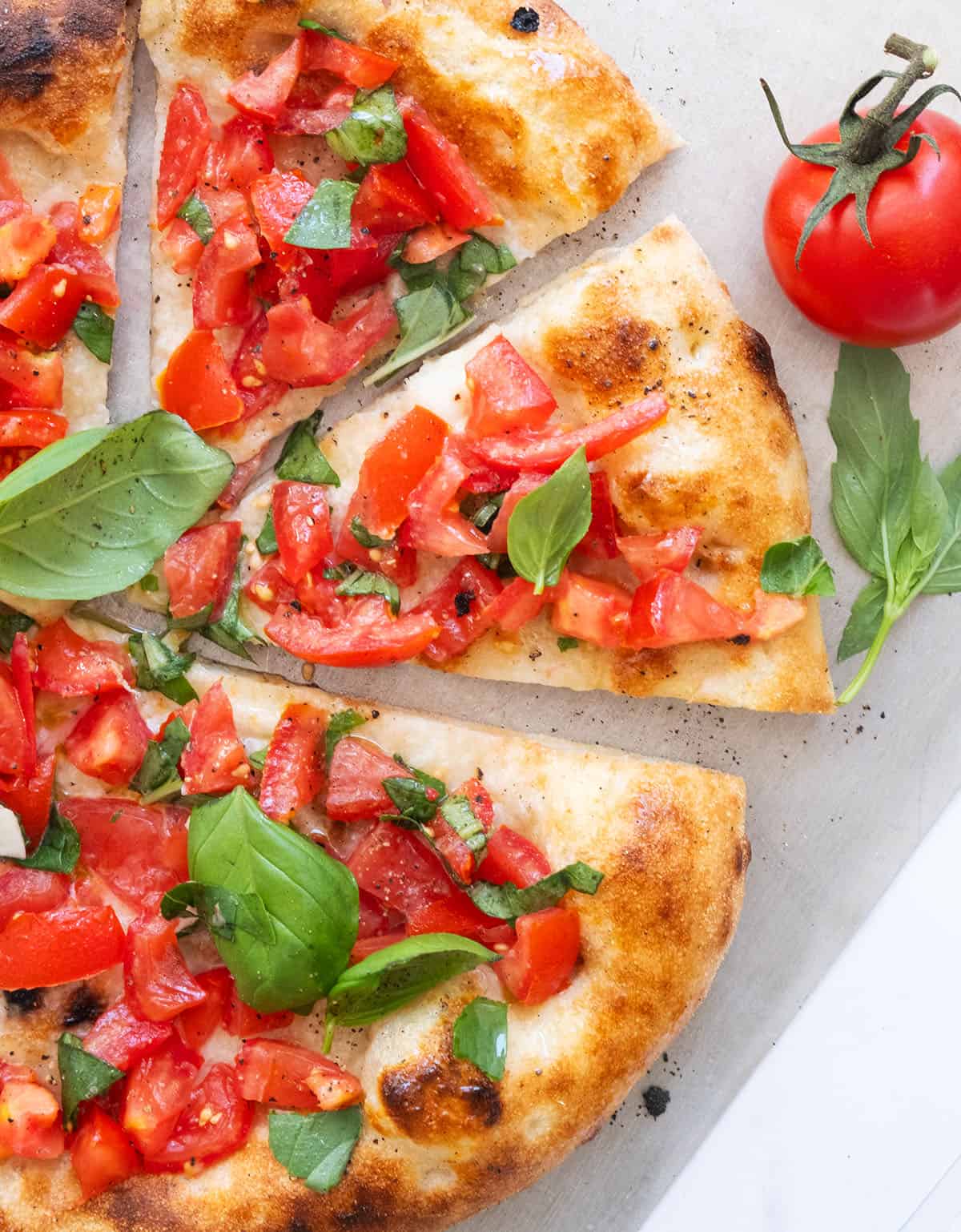 Top view of a round bruschetta pizza topped fresh basil leaves and cut into slices.