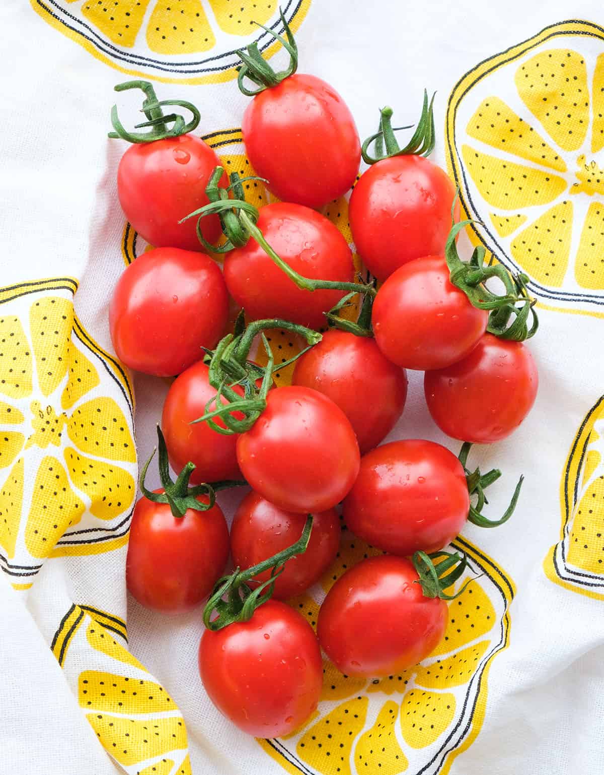 Top view of some cherry tomatoes on a white and yellow dish towel. 