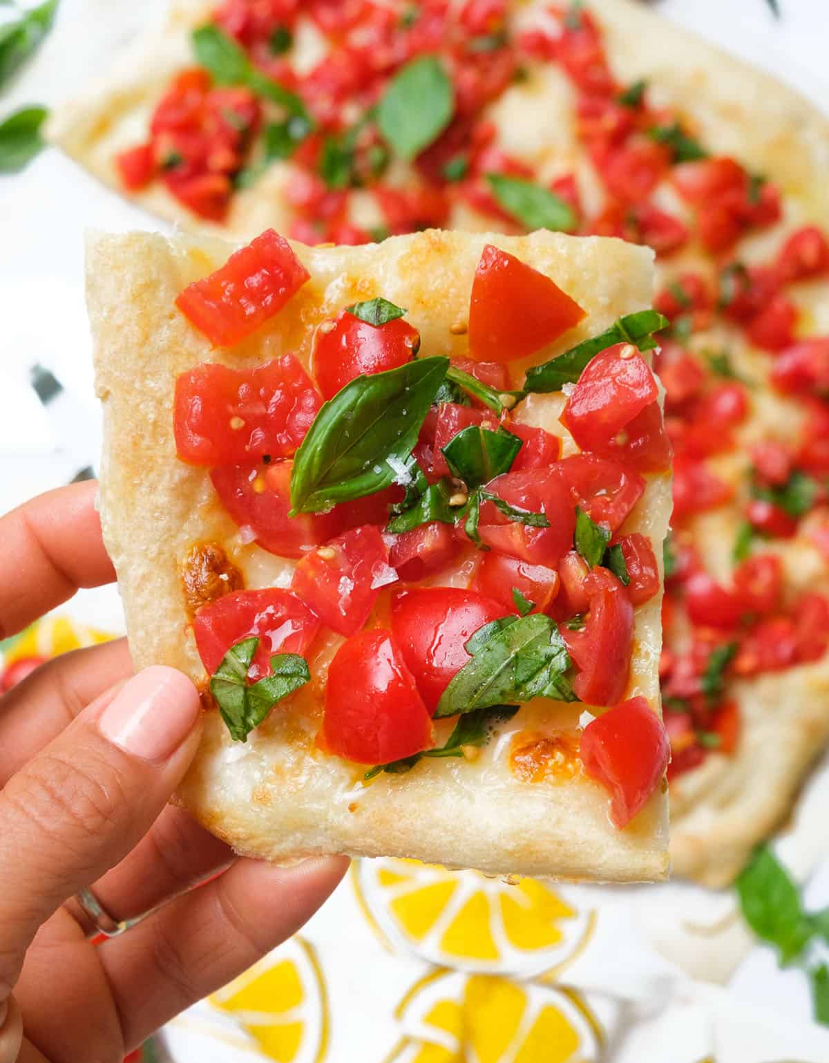 Close-up of a slice of bruschetta pizza topped with juicy fresh tomatoes and fresh basil leaves.