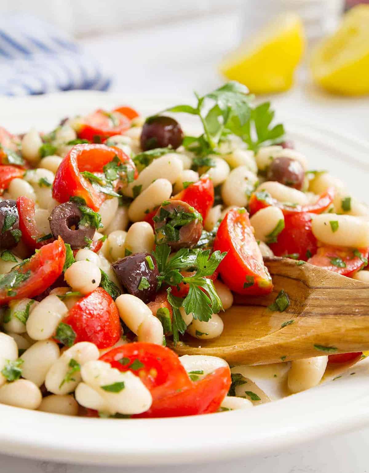 Close-up of a white plate full of cannellini bean salad with tomatoes and olives.