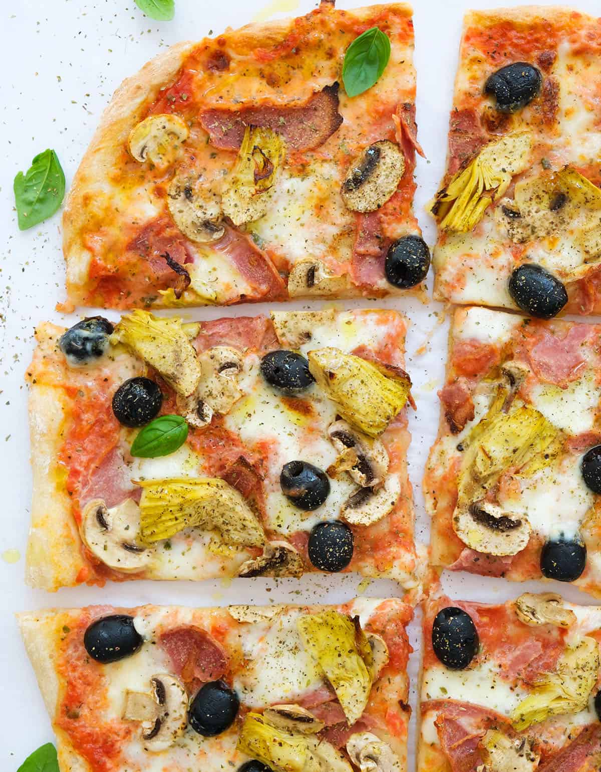 Top view of a large capricciosa pizza cut into slices over a white background.