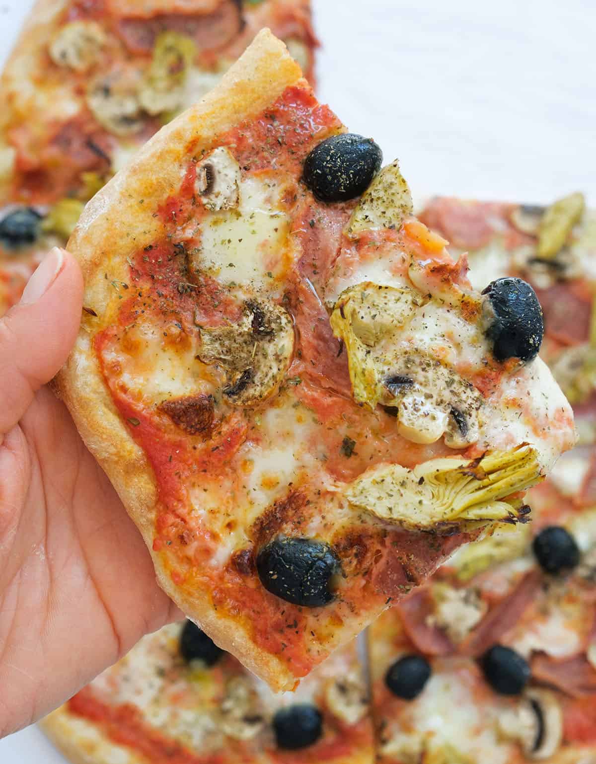 Close-up of a lice of capricciosa pizza topped with black olives, mushrooms and artichokes.