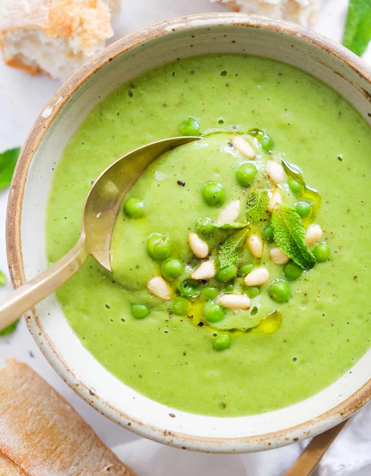 Top view of a bowl full of creamy green pea soup garnished with peas and pine nuts.