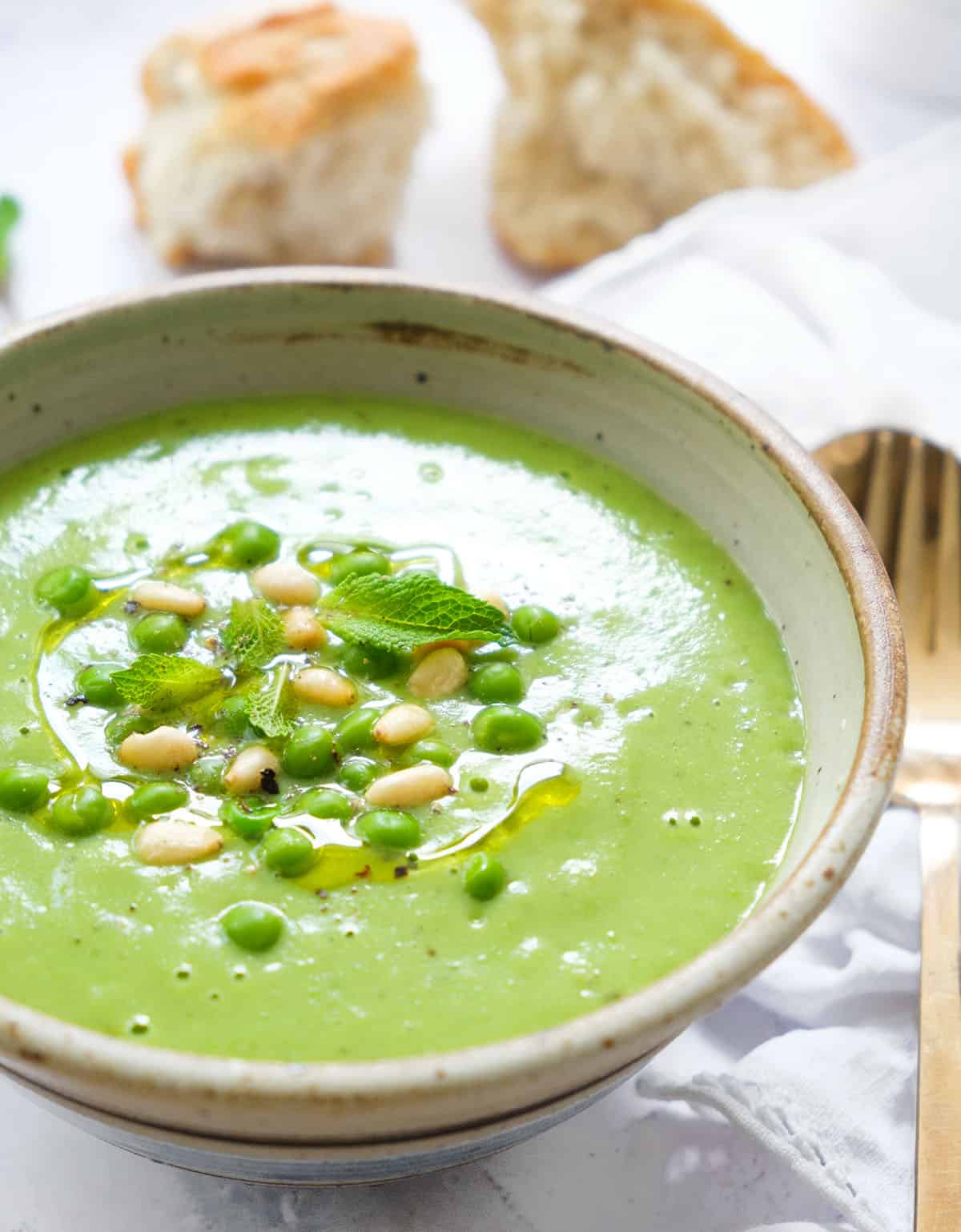 Close-up of a grey bowl full of green pea soup with some crusty bread in the background.