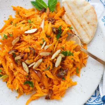 Top view of a white plate full of Moroccan carrot salad served with pita bread.