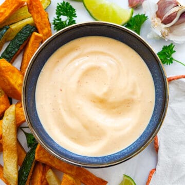 Top view of a blue bowl full of sriracha aioli served with sweet potatoes chips and lime wedges.