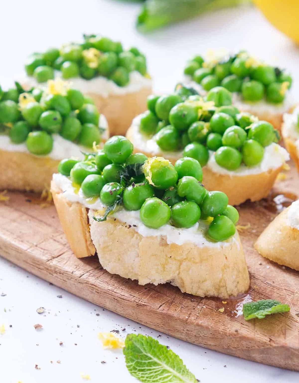 Close-up of a wooden board full of summer appetizers made with crostini, ricotta and green peas.