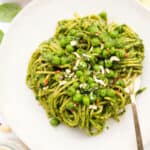 Close-up of a white plate full of healthy spaghetti with peas and green pesto.