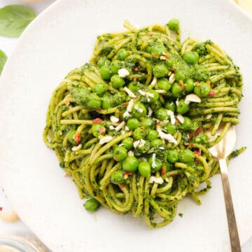 Close-up of a white plate full of healthy spaghetti with peas and green pesto.