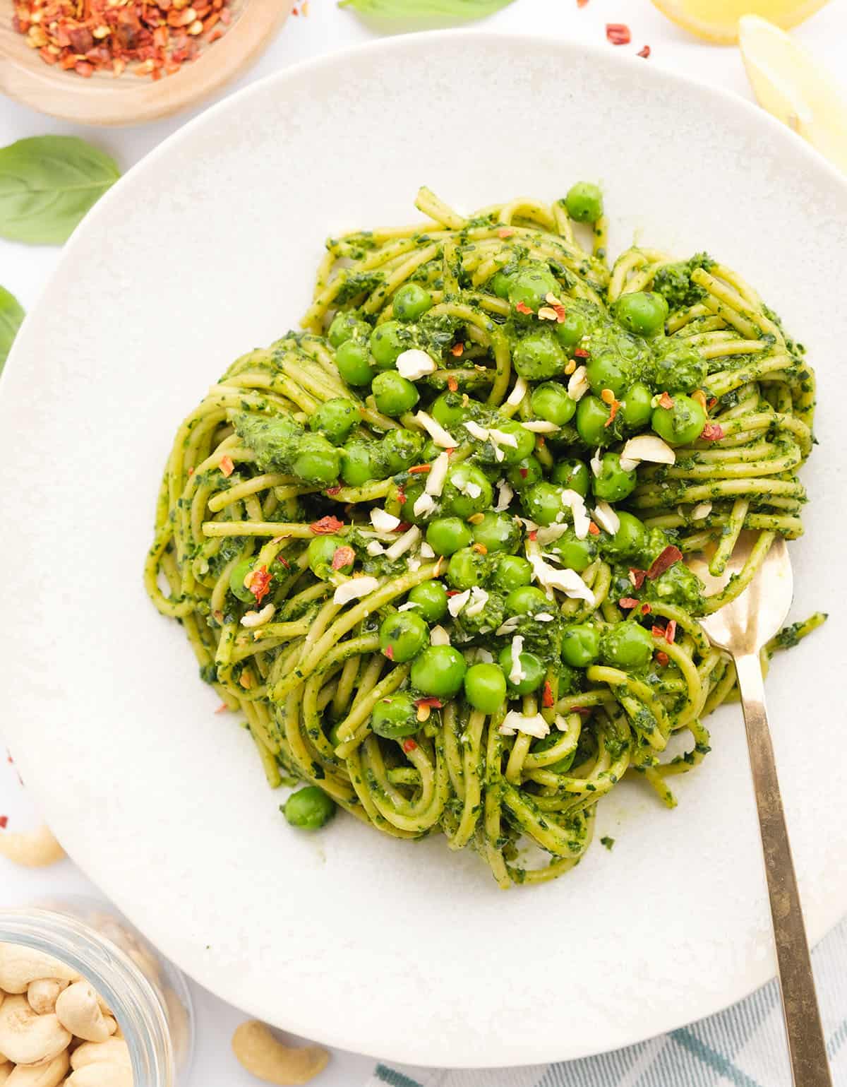 Top view of a white plate full of healthy spaghetti with a green pesto and peas.