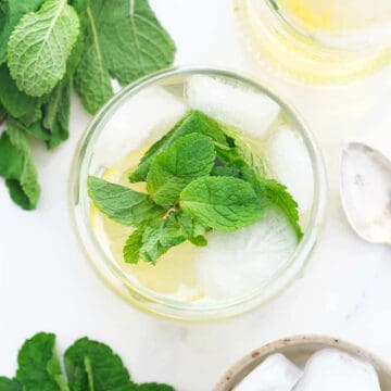 Top view of a glass full of mint syrup, ice and mint leaves over a white background.