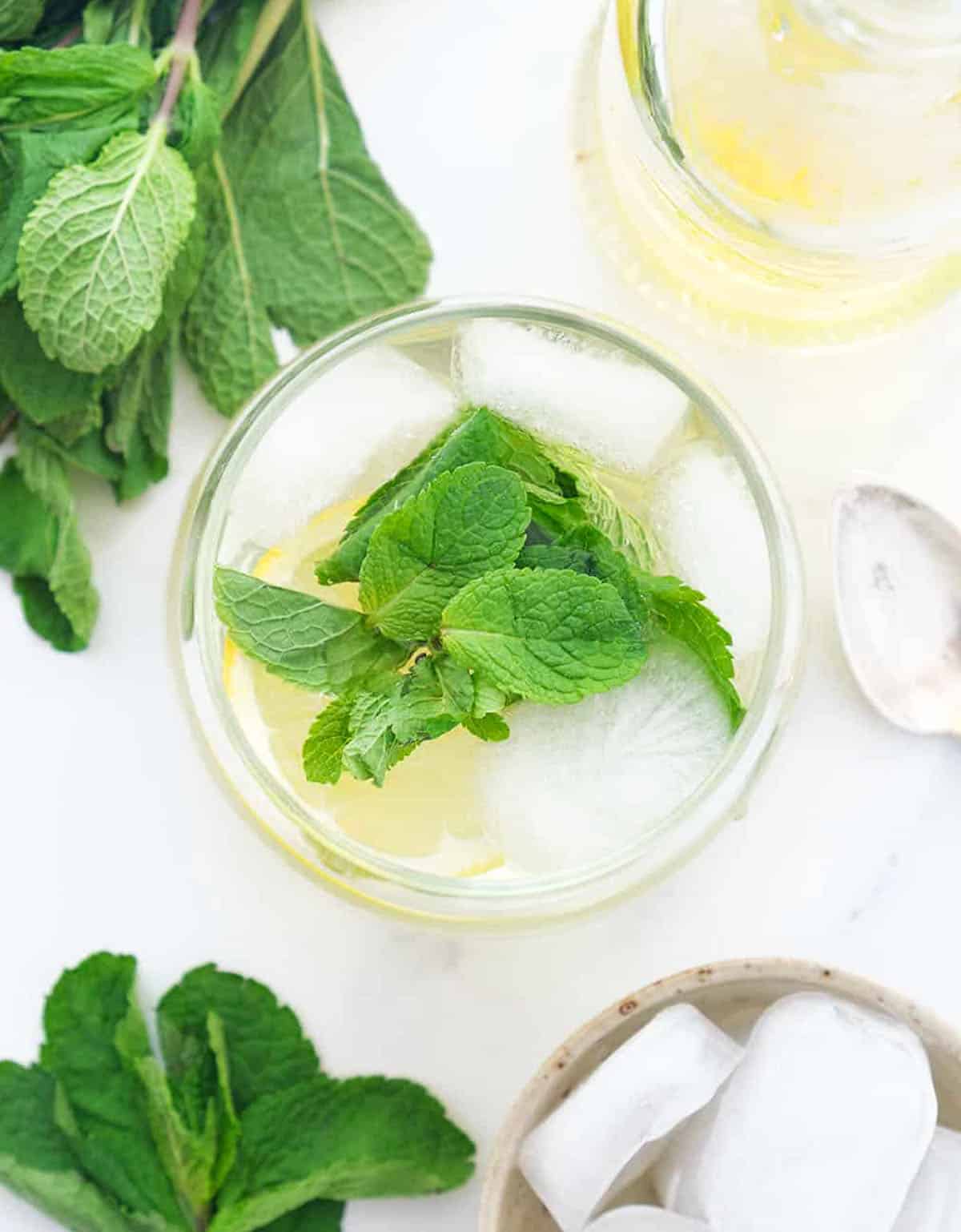 Top view of a glass full of mint syrup, ice and mint leaves over a white background.