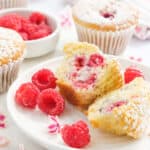 A few raspberry muffins on a white plate over a white background served with fresh raspberries.
