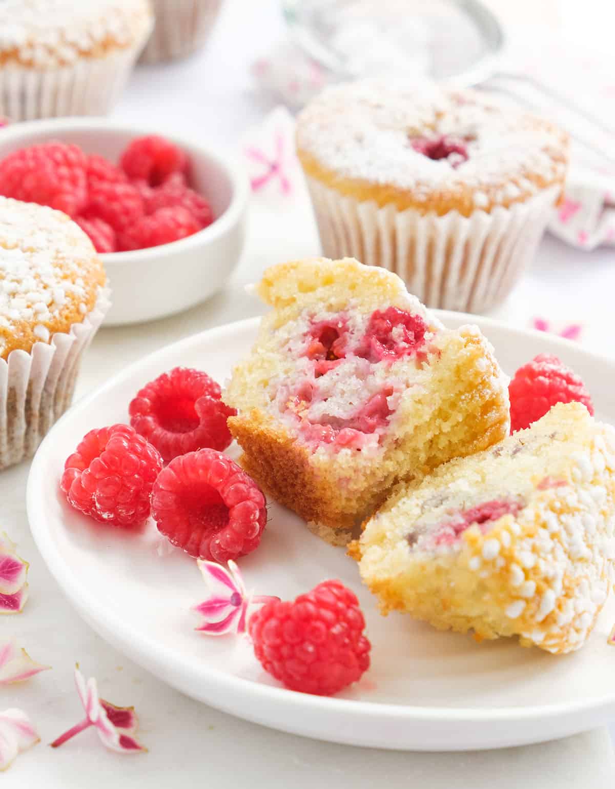 Close-up of a few raspberry muffins on a white plate served with extra fresh raspberries. 