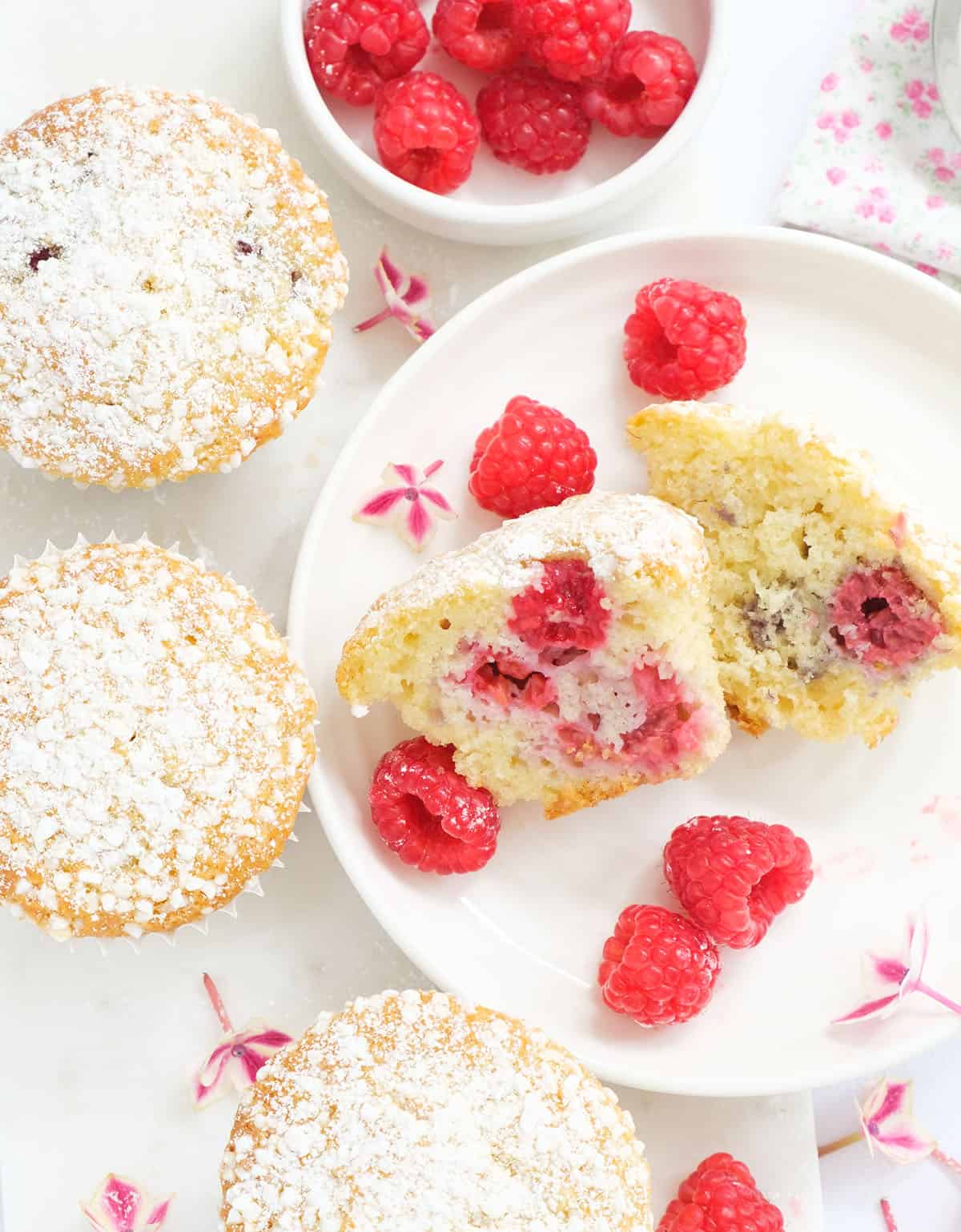 Top view of a few muffins on a white background showing their moist texture packed with juicy raspberries.