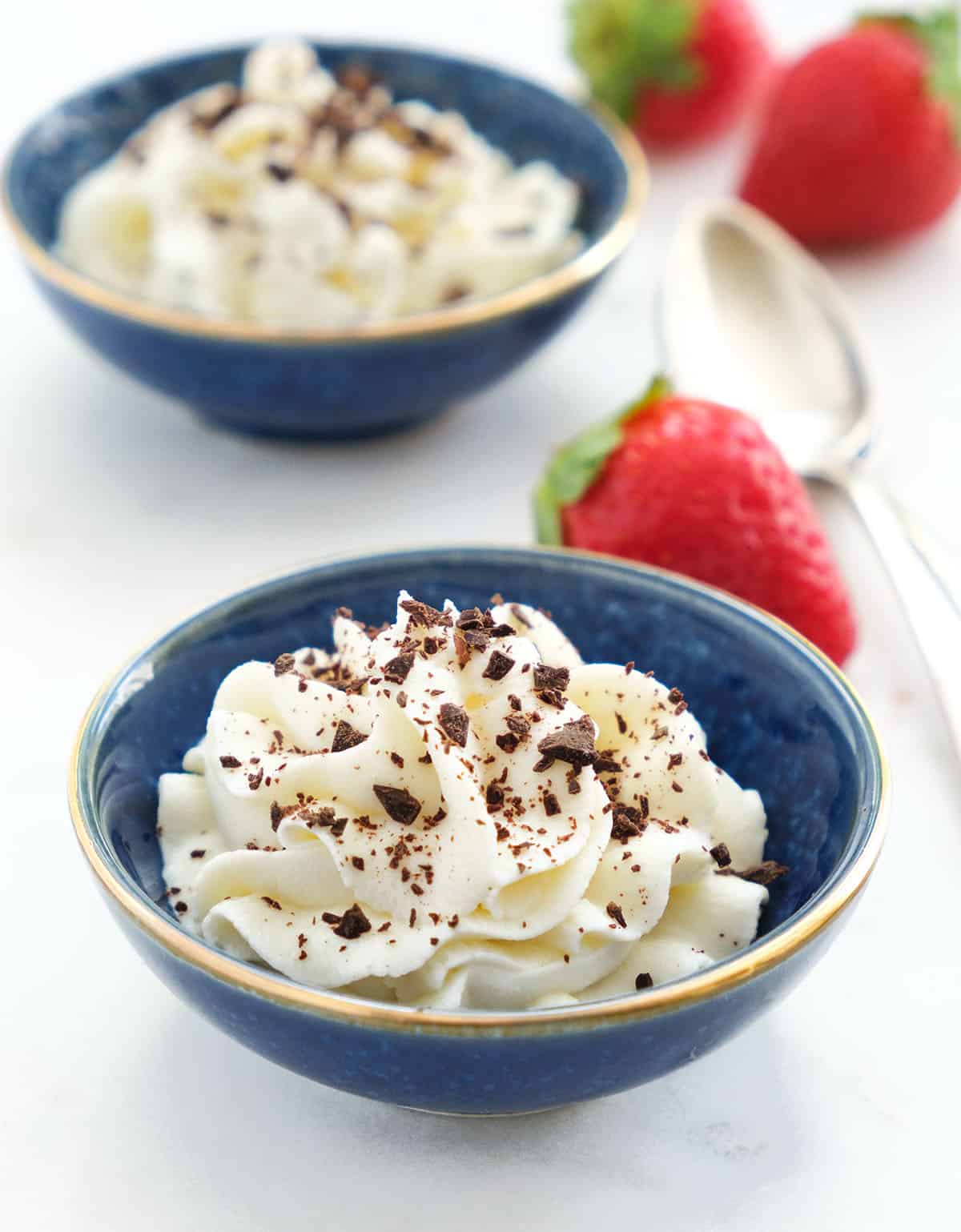 Two small blue bowl full of ricotta cream garnished with chocolate bits and served with strawberries.