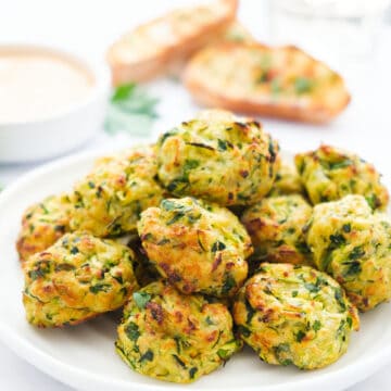 Some crispy zucchini bites on a white plate over a white background.