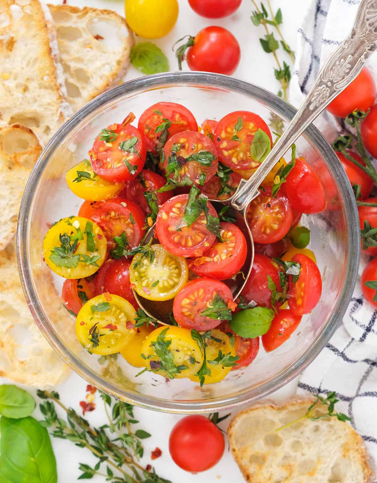 Top view of a glass bowl full of marinated cherry tomatoes served with crostini.