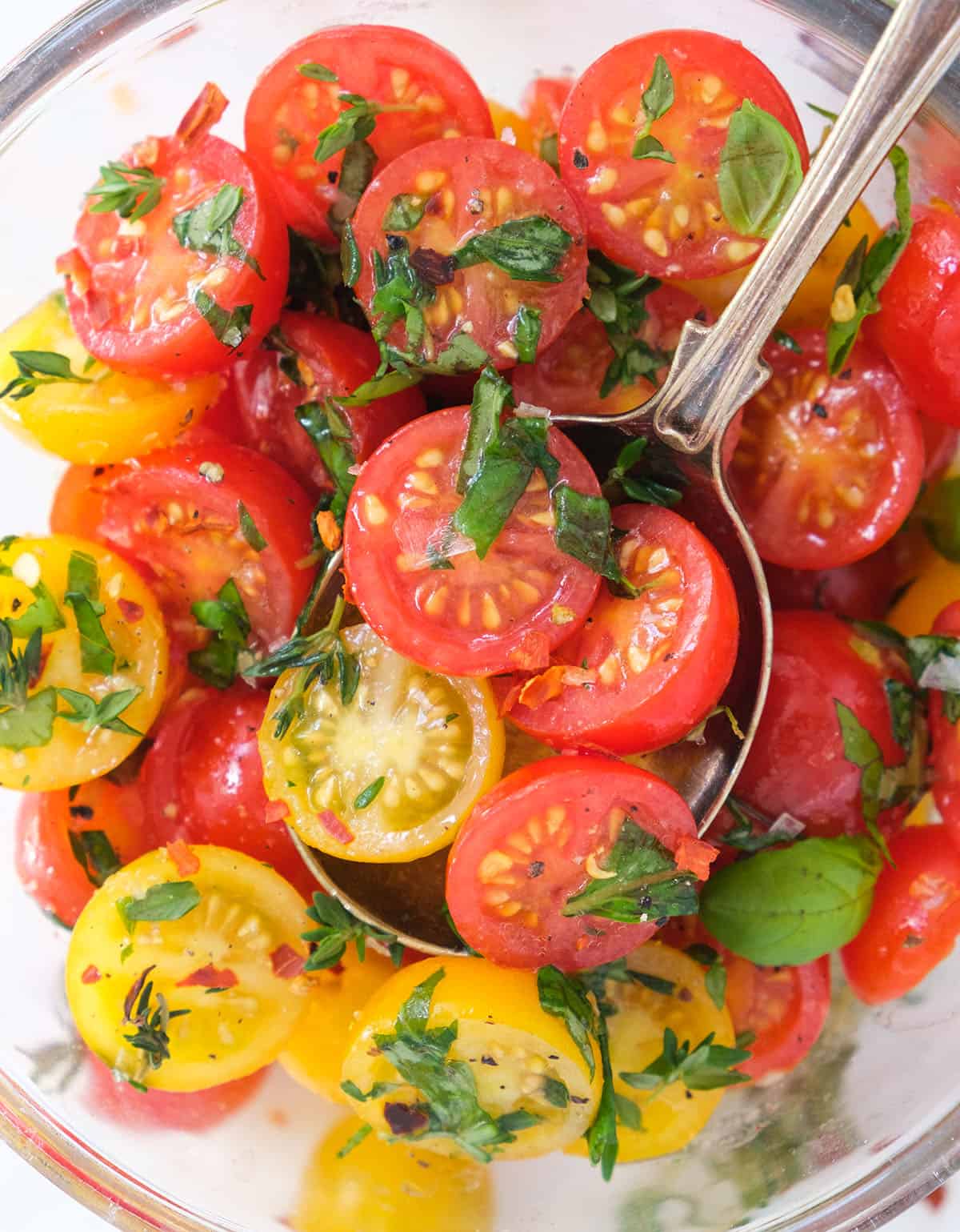 Top view of a glass bowl full of marinated cherry tomatoes with fresh basil.