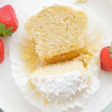 A white plate with one of the ricotta muffins cut into halves and showing its tender texture.