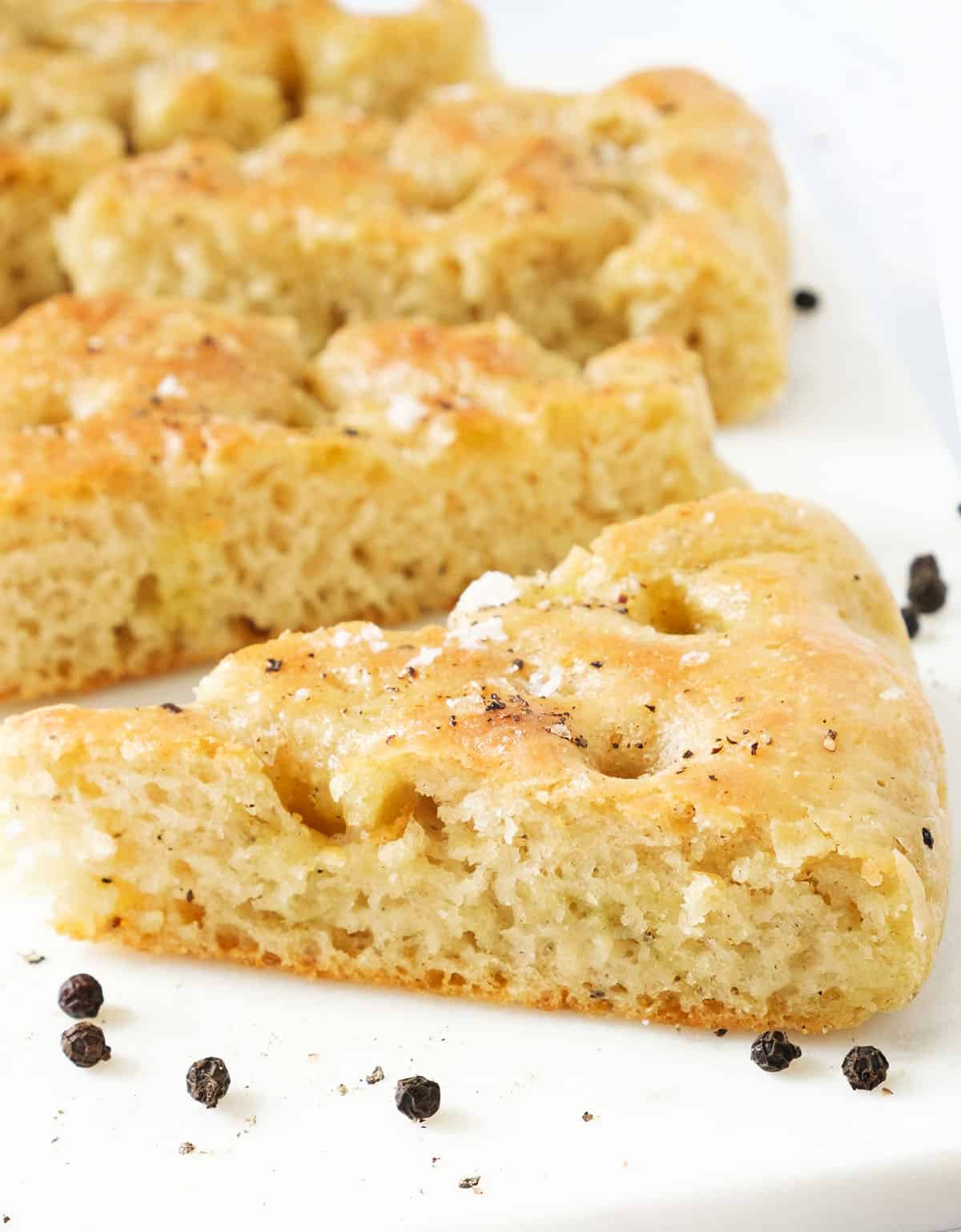 Close-up of a few slices of black pepper focaccia over a white background.