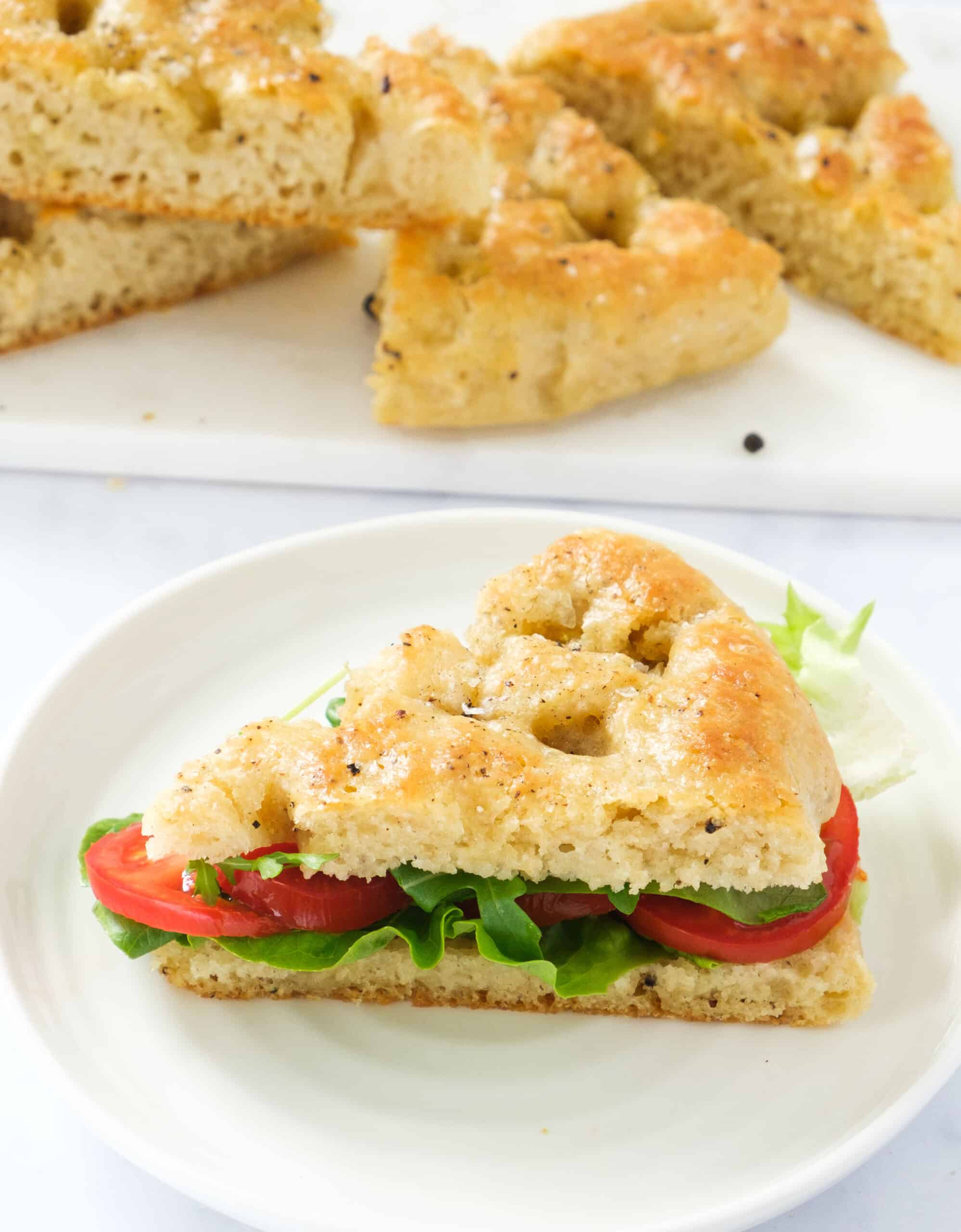 Close-up of a slice of black pepper focaccia stuffed with lettuce salad and tomato slices.