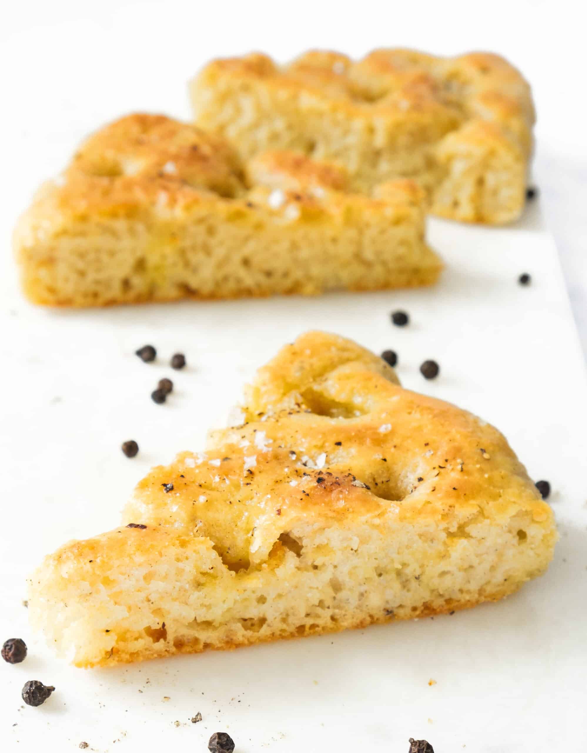 Close-up of a few slices of black pepper focaccia over a white background.