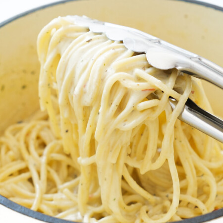 Close-up of some creamy spaghetti over a white pot and white background.
