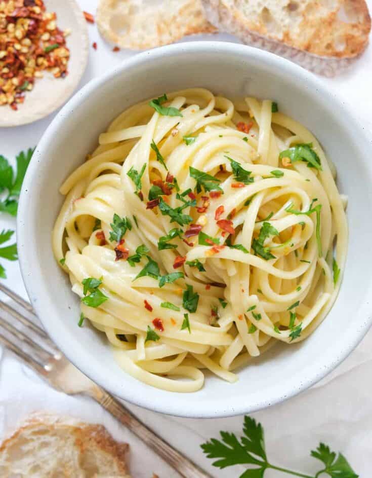 Top view of a white bowl full of garlic butter pasta garnished with parsley and chili flakes.