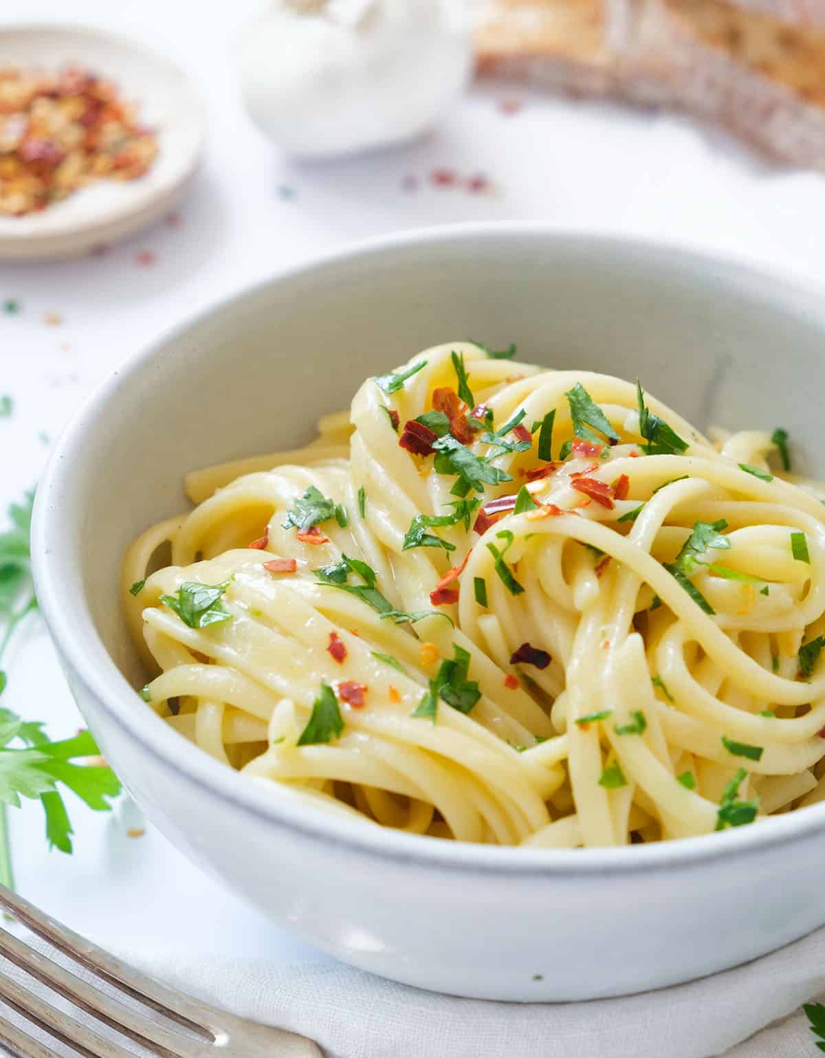Close-up of a white bowl full of pasta with butter and garlic.