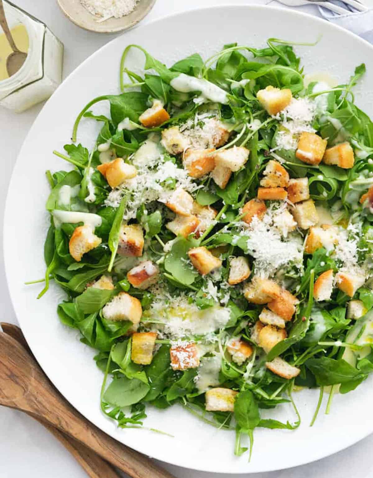 Top view of a large salad plate full of spinach arugula salad topped with parmesan and croutons.