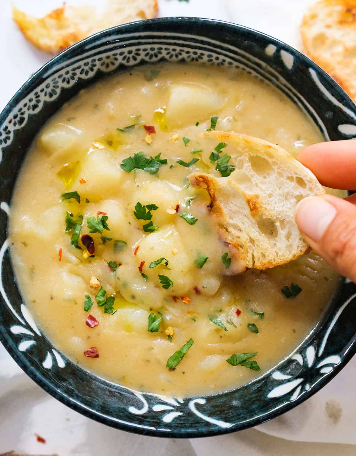 Close-up of a slice of crusty bread dunking into the vegan potato soup.