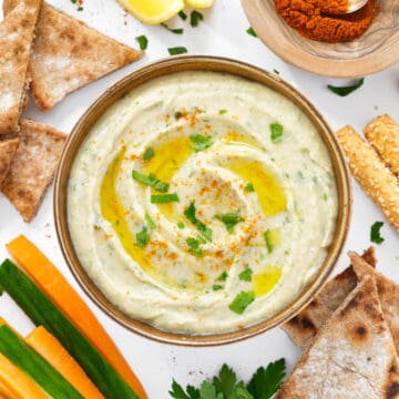 Top view of a small bowl full of white bean dip served with pita bread and veggies.